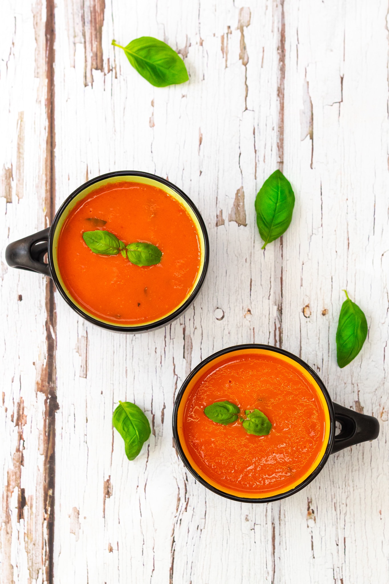 two bowls of tomato soup with basil leaves