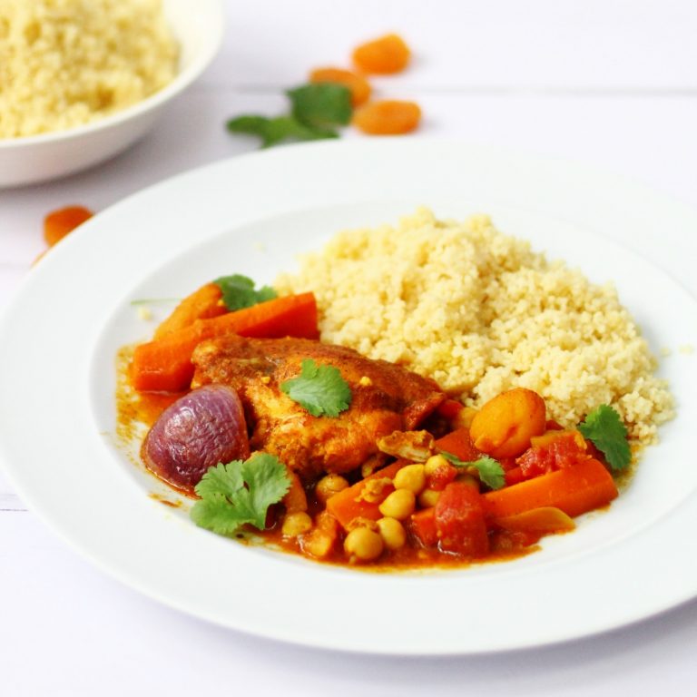 Plate of chicken tagine with couscous and apricots in the background