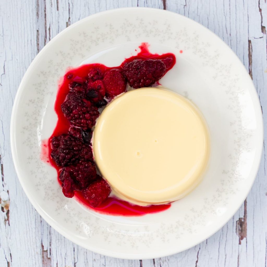 Vanilla panna cotta on a plate with a red berry sauce