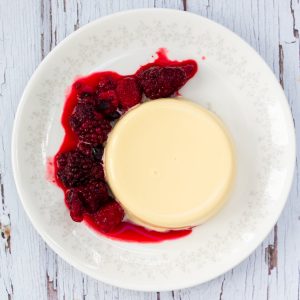 Vanilla panna cotta on a plate with a red berry sauce