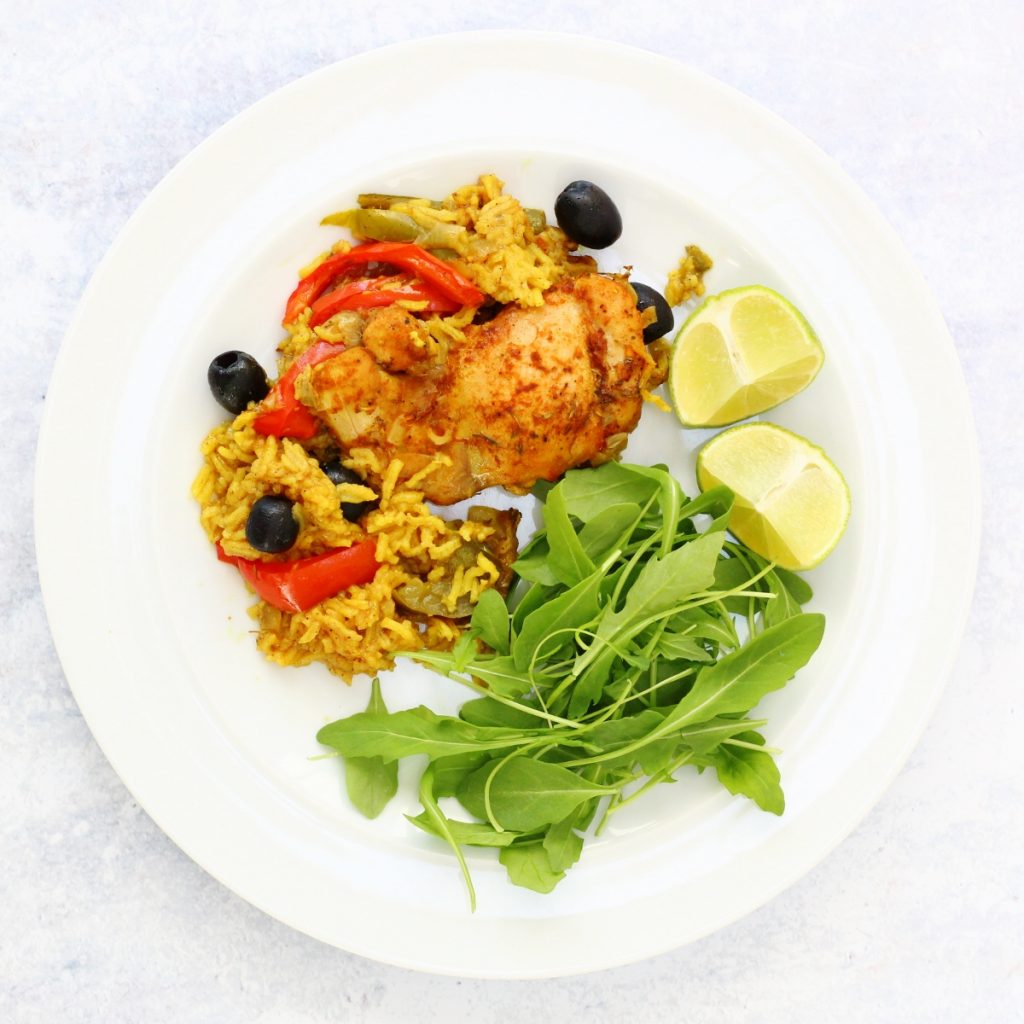 Plate of chicken cooked in spicy rice with salad leaves and lime