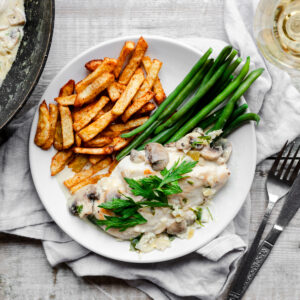 Plate of chicken in a creamy mushroom sauce with chips and green beans