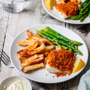 Chorizo crusted cod on a plate with chips and asparagus
