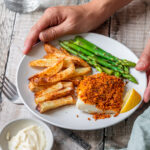 hands holding plate of cod with chorizo breadcrumbs