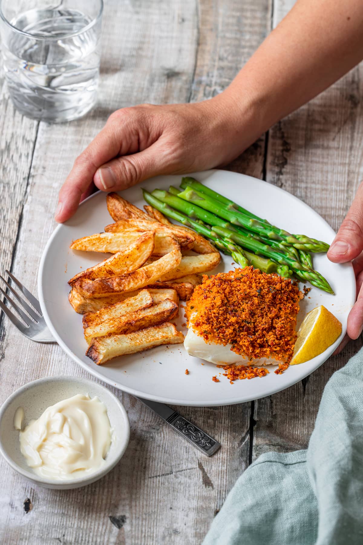 hands holding plate of cod with chorizo breadcrumbs