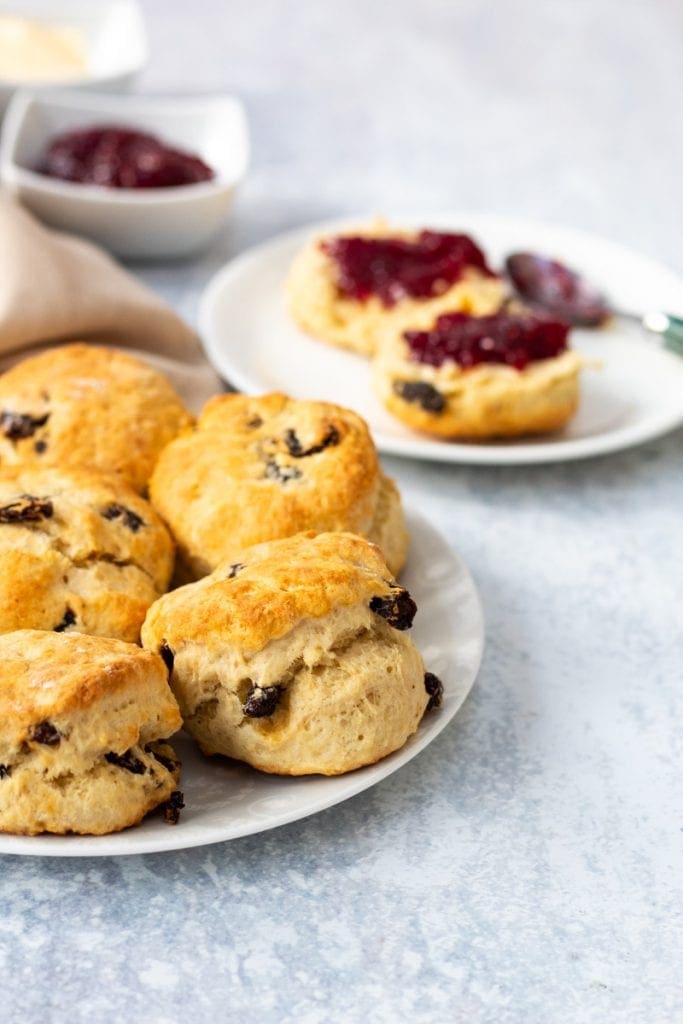 plate of fruit scones with jam on a scone in background