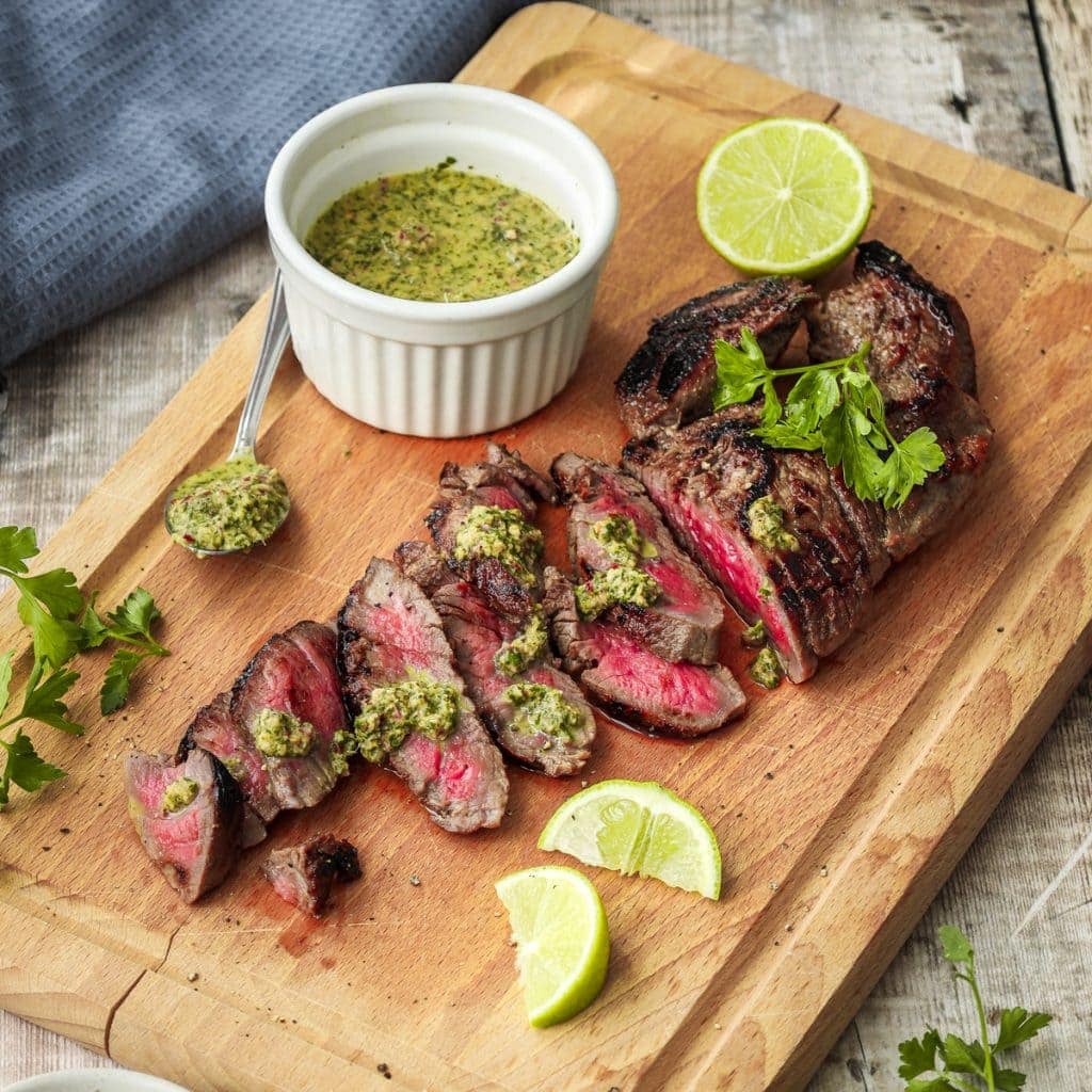 Honey lime marinated steak on a chopping board with chimichurri