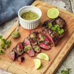 Honey lime marinated steak on a chopping board with chimichurri