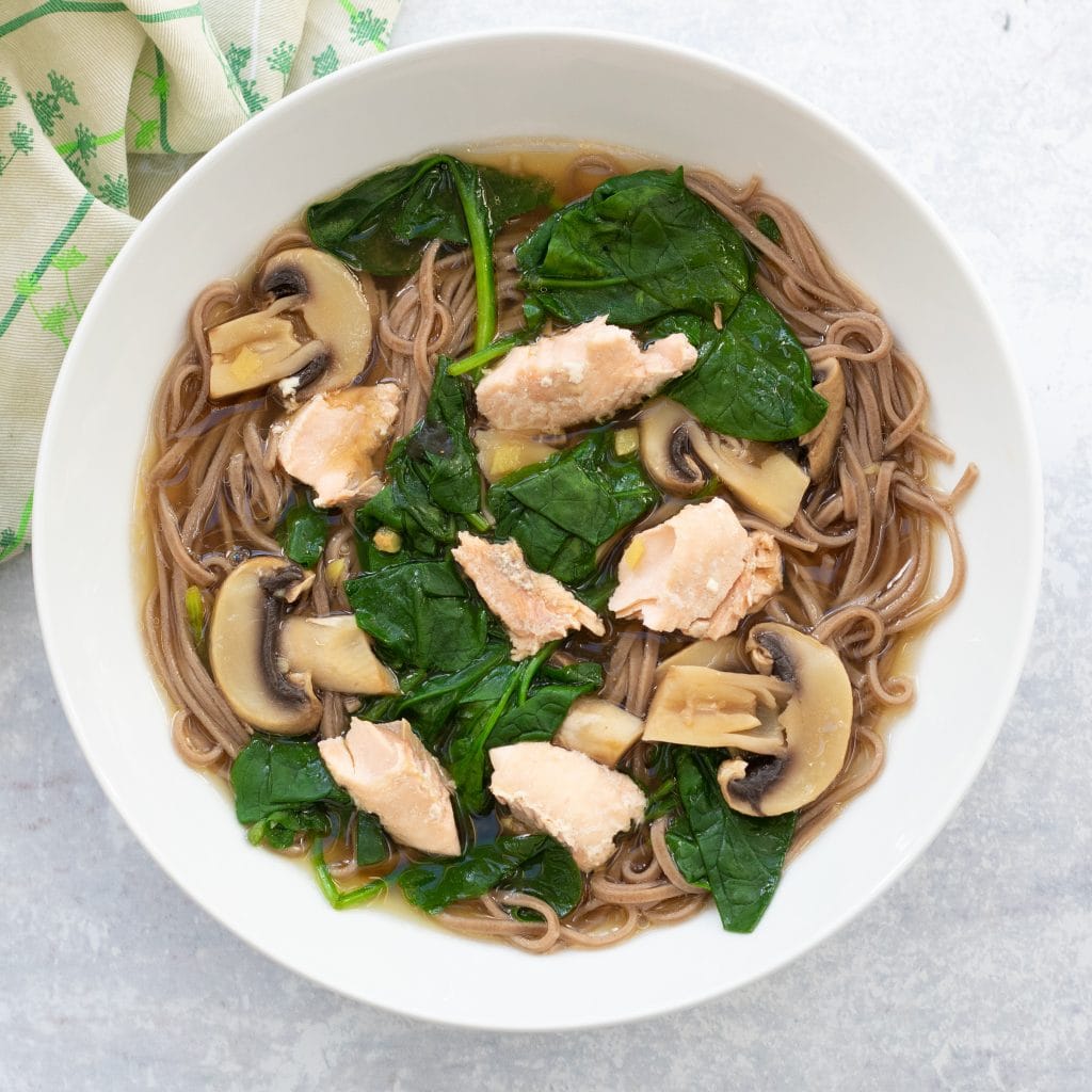 bowl of salmon miso soup with soba noodles, spinach and mushrooms