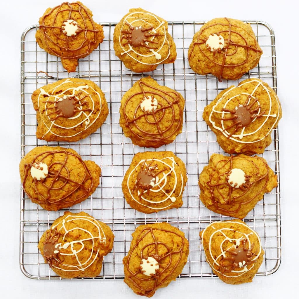 Pumpkin cookies on a cooling rack, decorated with chocolate spiders and webs