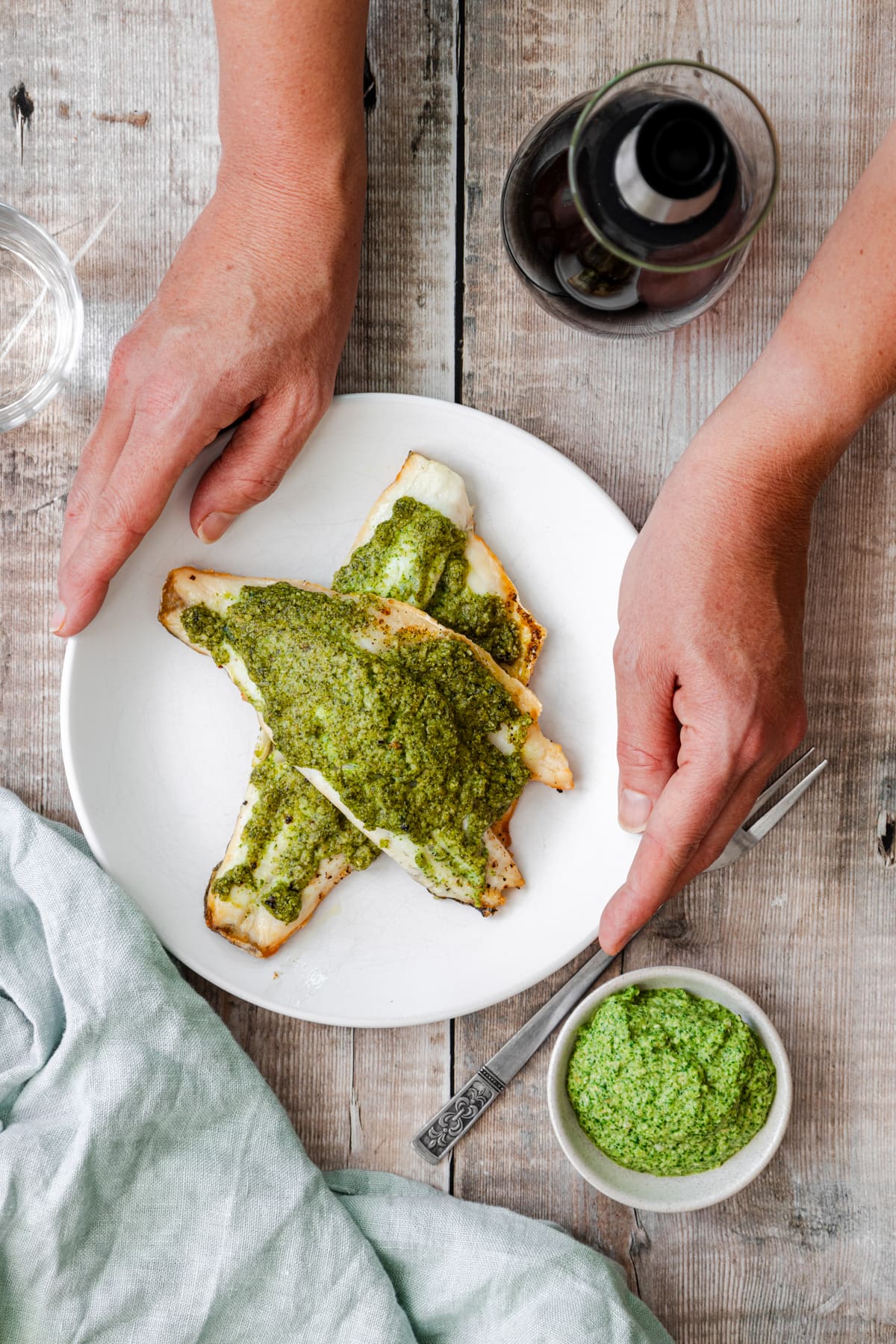hands holding a plate of sea bass coated in pesto