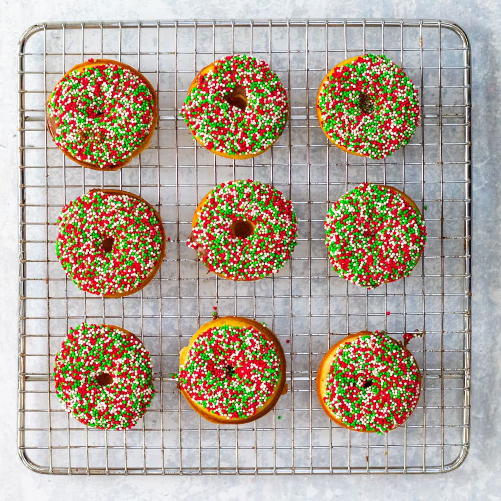 Baked Christmas doughnuts on a wire rack with sprinkles and chocolate
