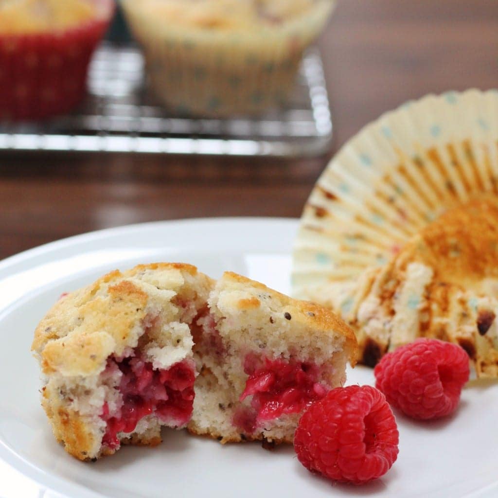 Lemon Raspberry and Chia Seed Muffins broken in half with fresh raspberries on a plate