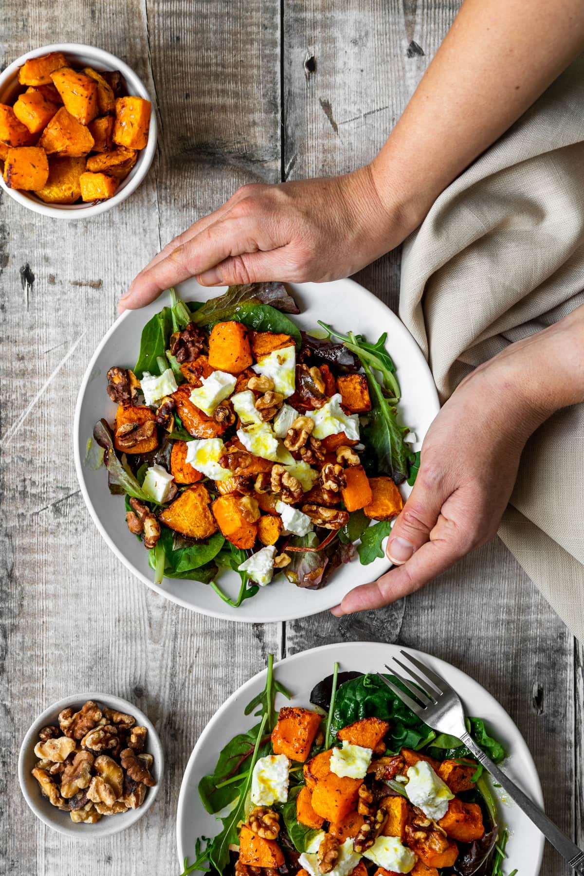 hands holding roasted butternut squash feta salad