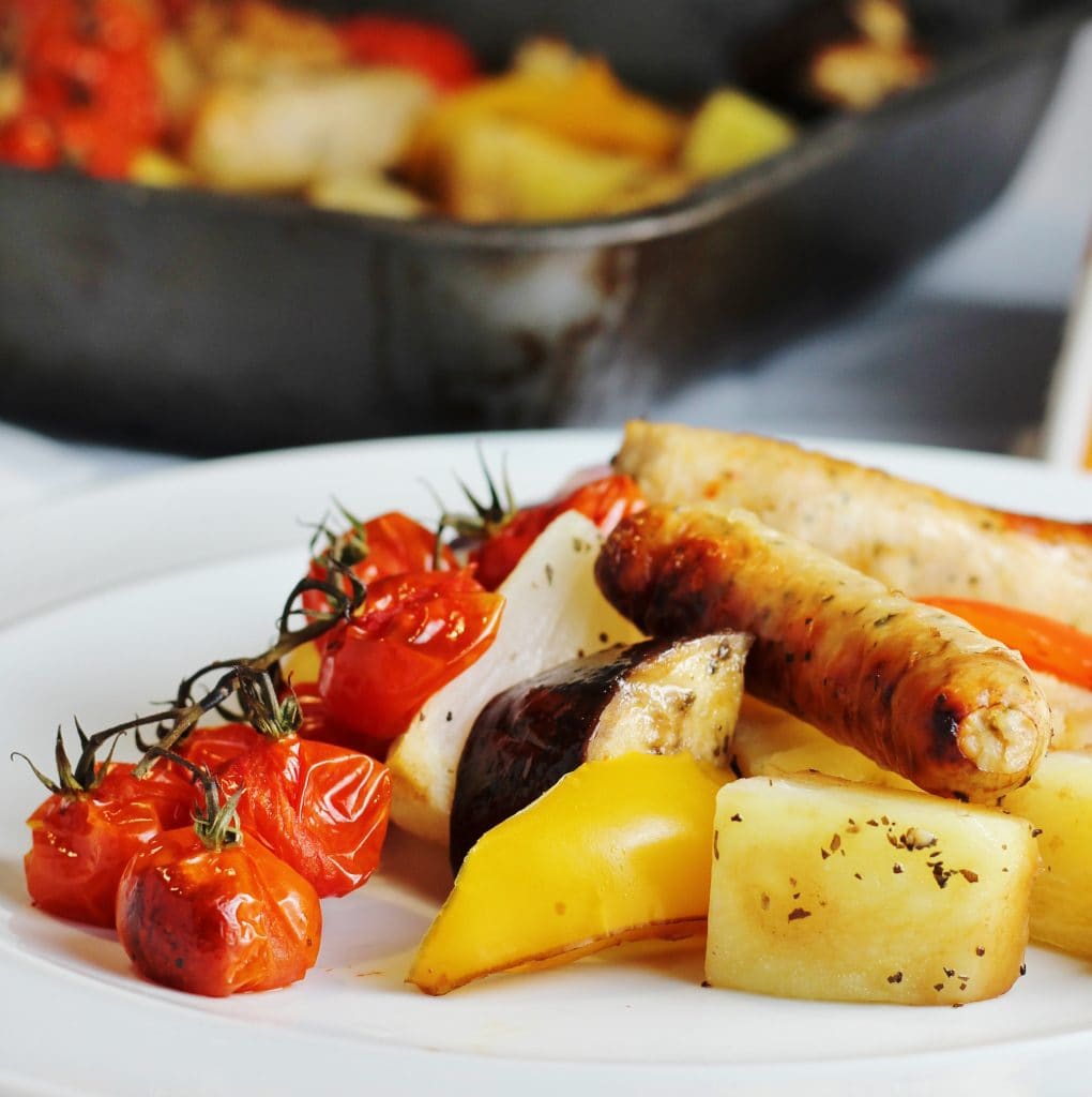 Close up of sausage tray bake on a plate showing sausages, tomatoes, potatoes, aubergine and peppers