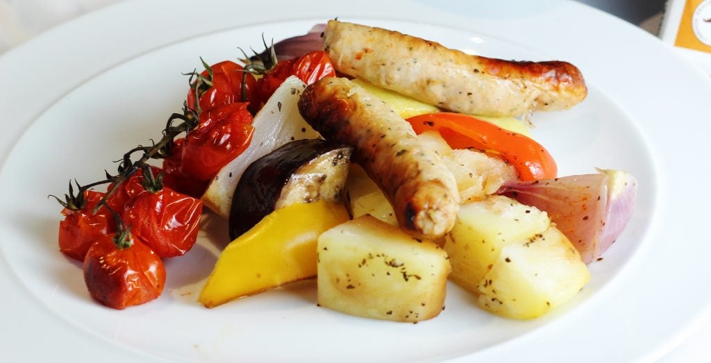 White plate with sausages, potatoes, tomatoes and roasted vegetables