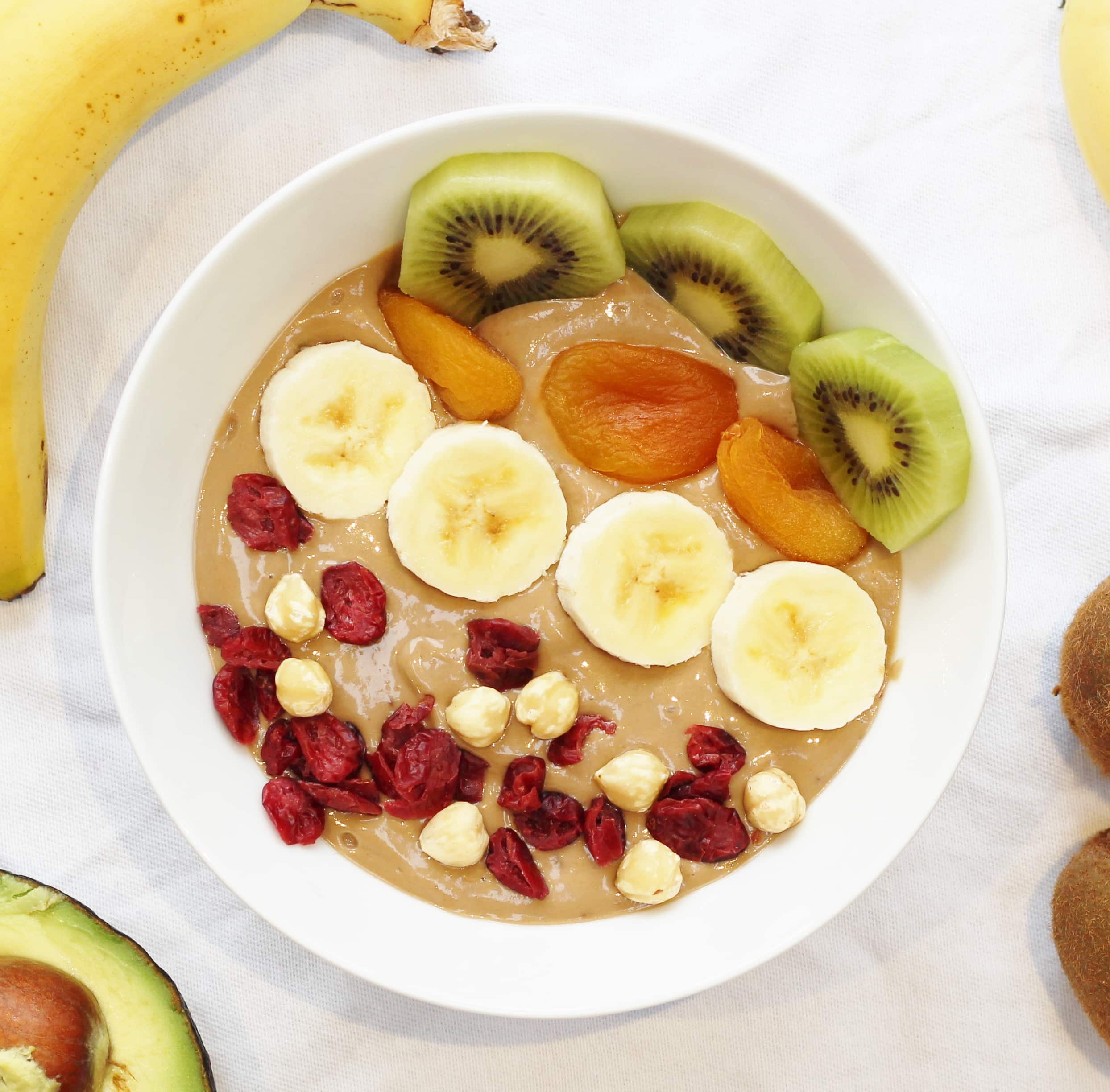 Healthy Nutella smoothie bowl with banana and avocado topped with banana, kiwi fruit, dried apricots, cranberries and hazelnuts