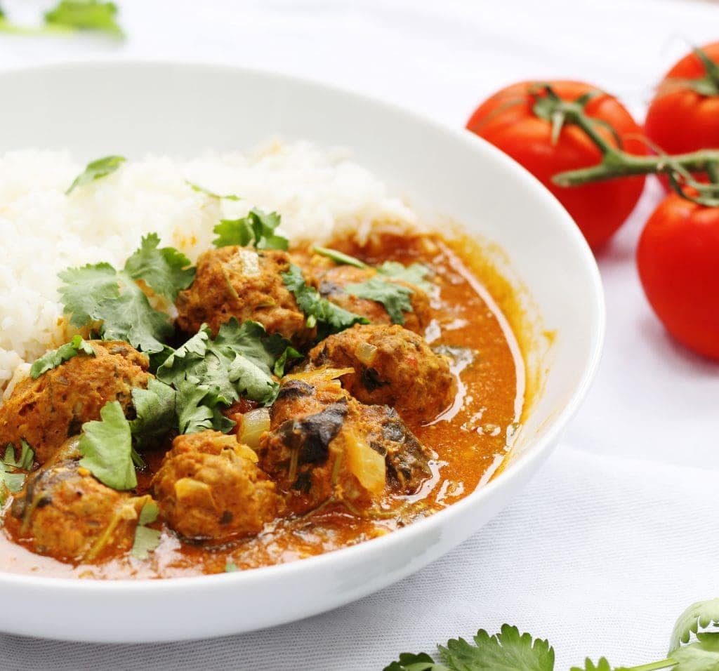 lamb meatball curry with tomatoes in background
