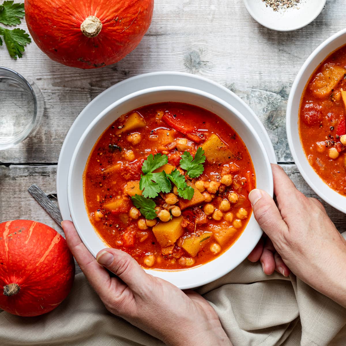 hands holding bowl of chickpea and pumpkin stew