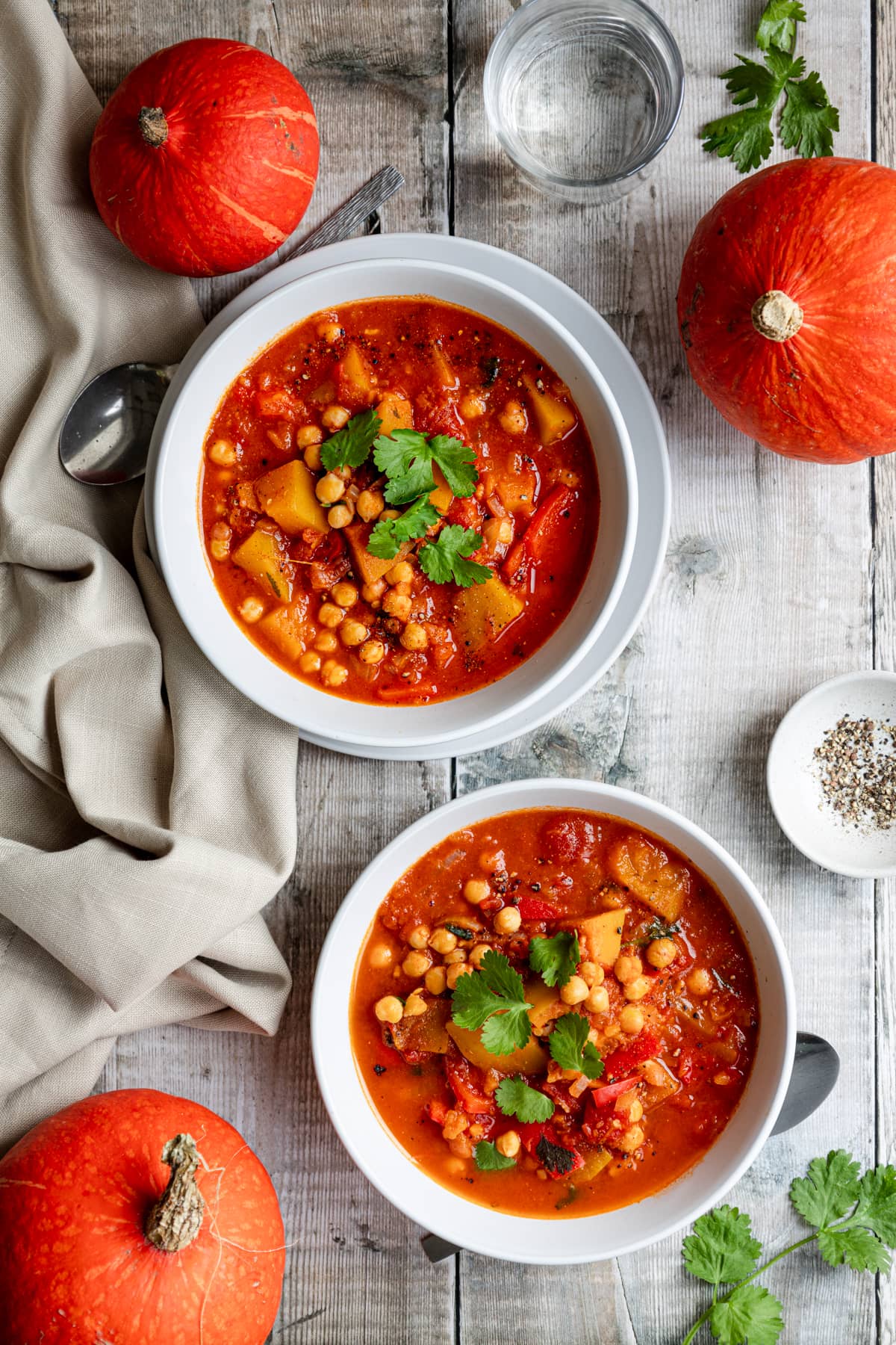 flatlay of two bowls of pumpkin chickpea stew with orange pumpkins