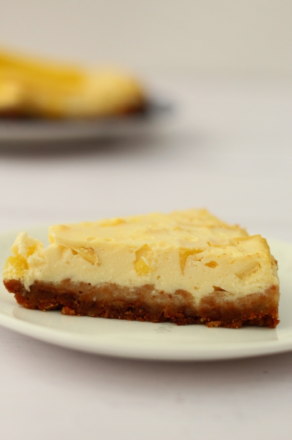 Slice of mango cheesecake with cheesecake in the background