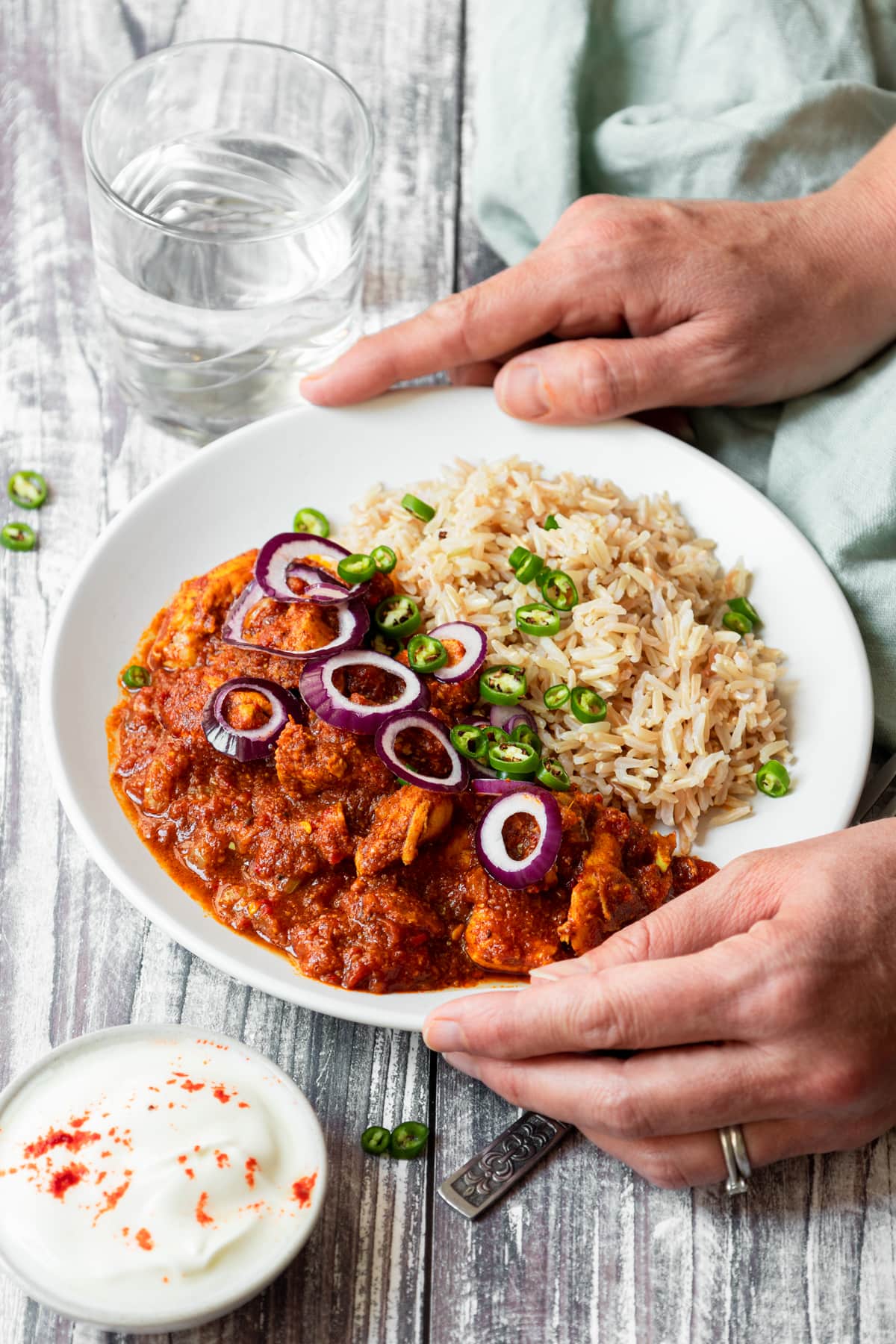 Hands holding plate of red Goan chicken with rice