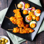 Spanish chicken kebabs on a black plate
