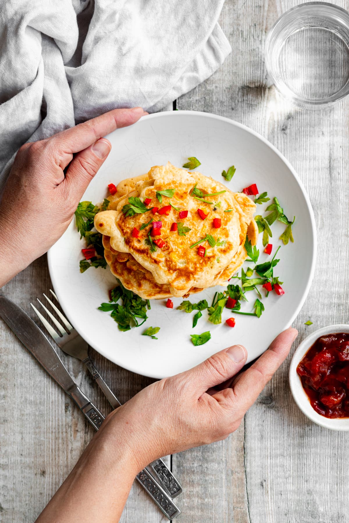 Hands putting down a plate of sweetcorn fritters