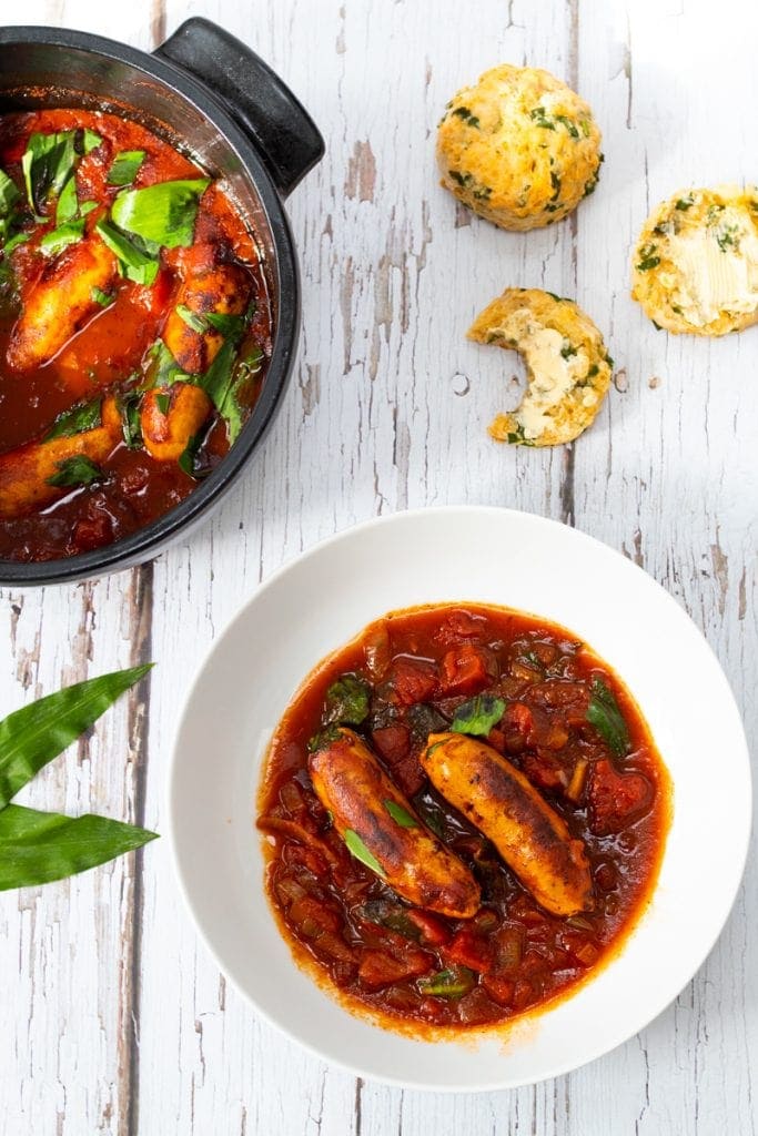 Wild garlic and sausage stew in a bowl with a pan and some scones