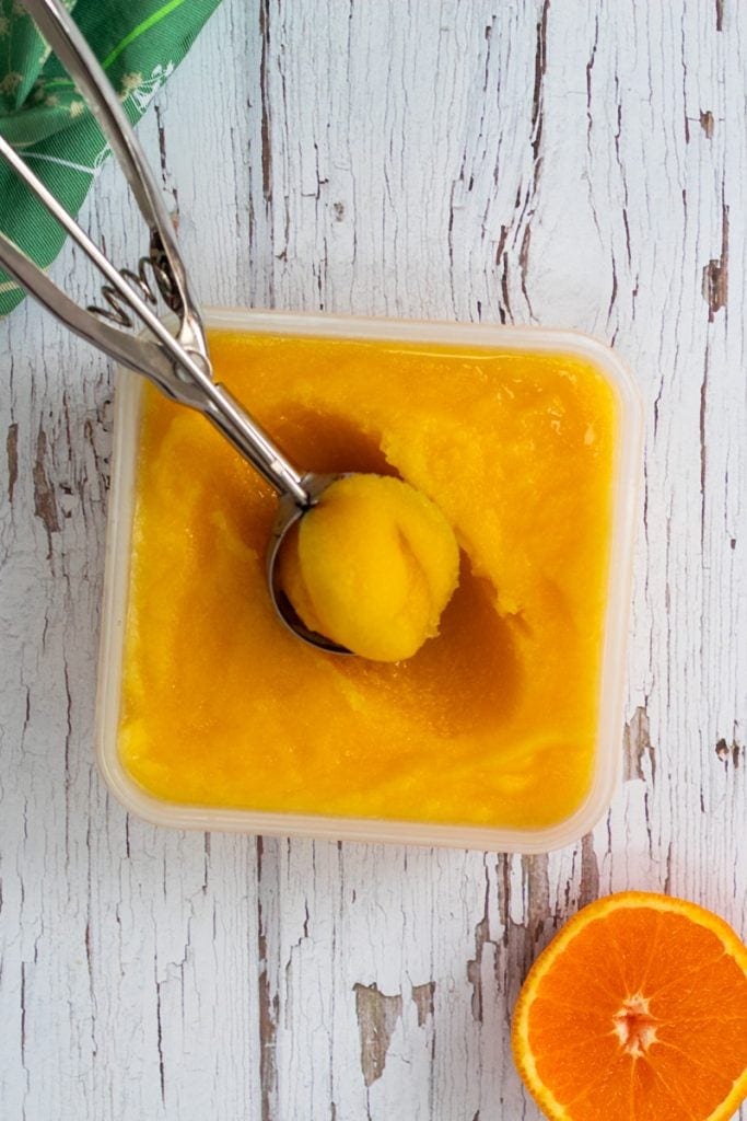 container of orange sorbet with an ice cream scoop of sorbet on top