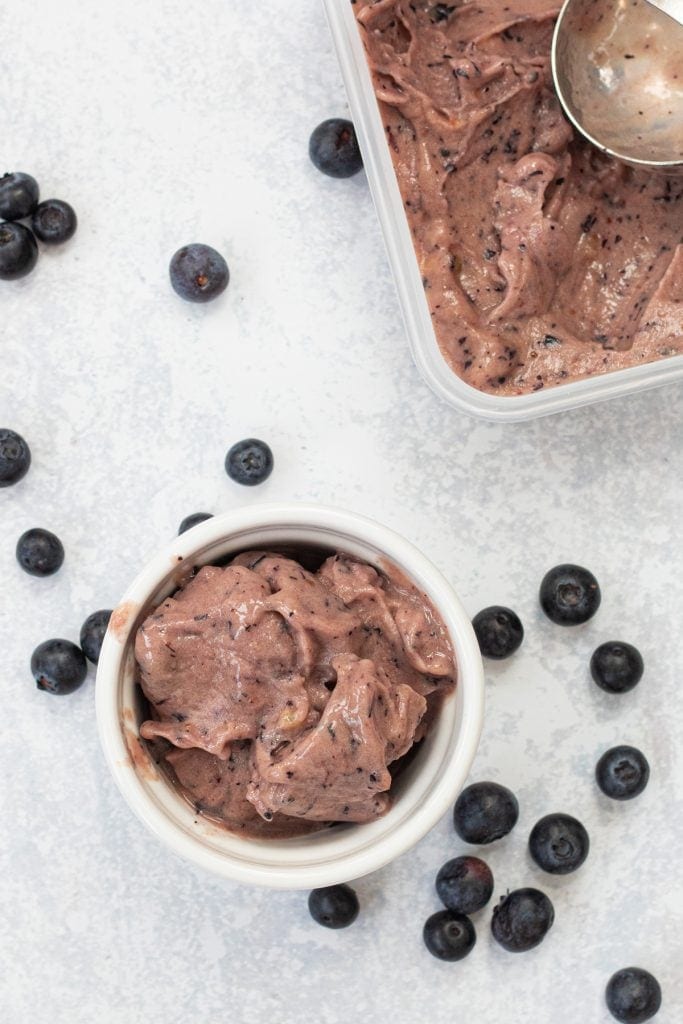 bowl of blueberry nice cream with tub of nice cream next to it