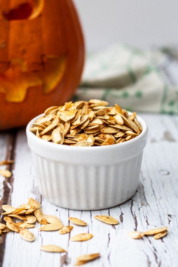 roasted pumpkin seeds in a bowl with a pumpkin in the background