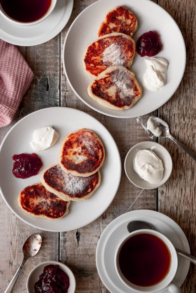 two plates of syrniki with coffee, jam and sour cream