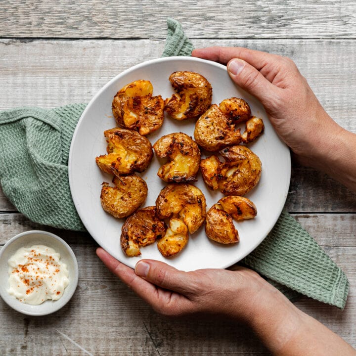 hands holding plate of spicy air fryer crushed potatoes